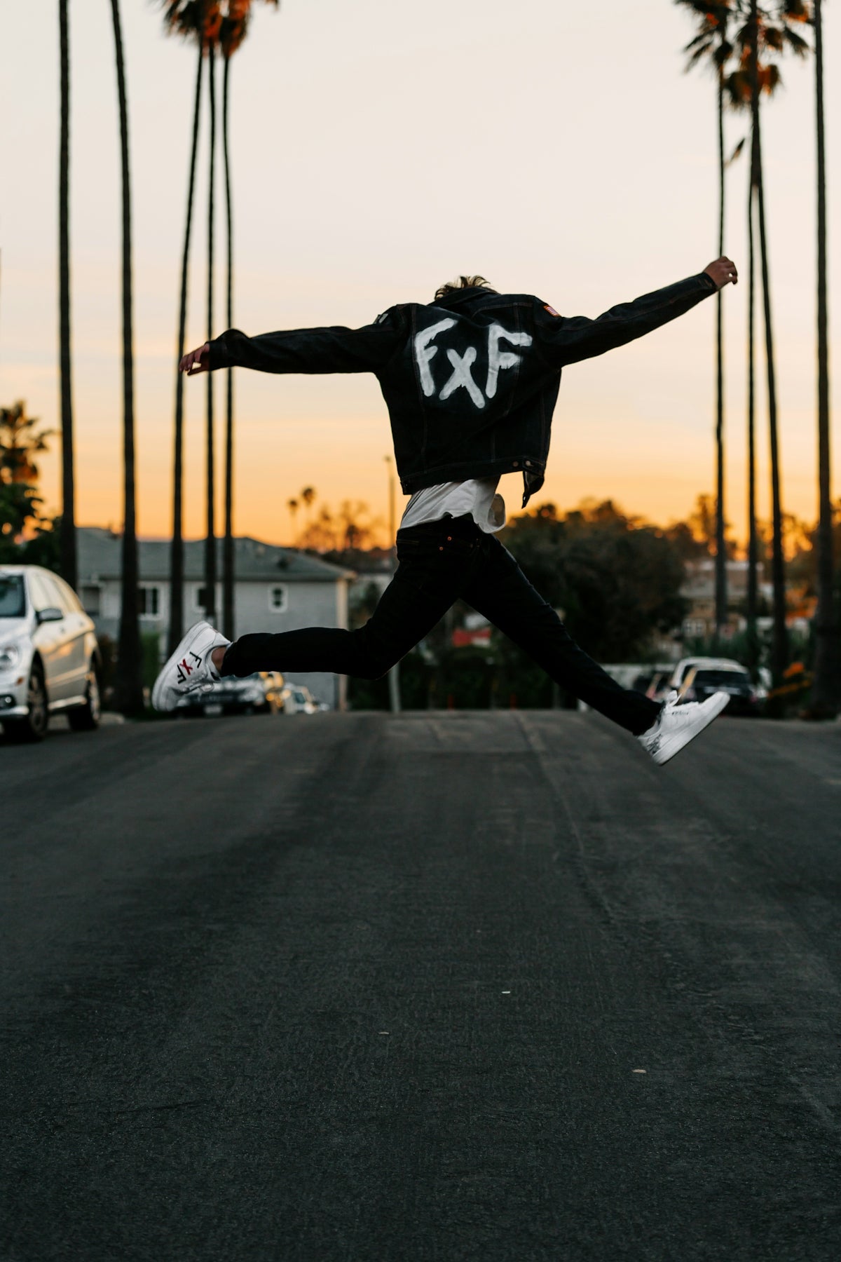 man in black and white jacket and black pants jumping on black asphalt road during daytime