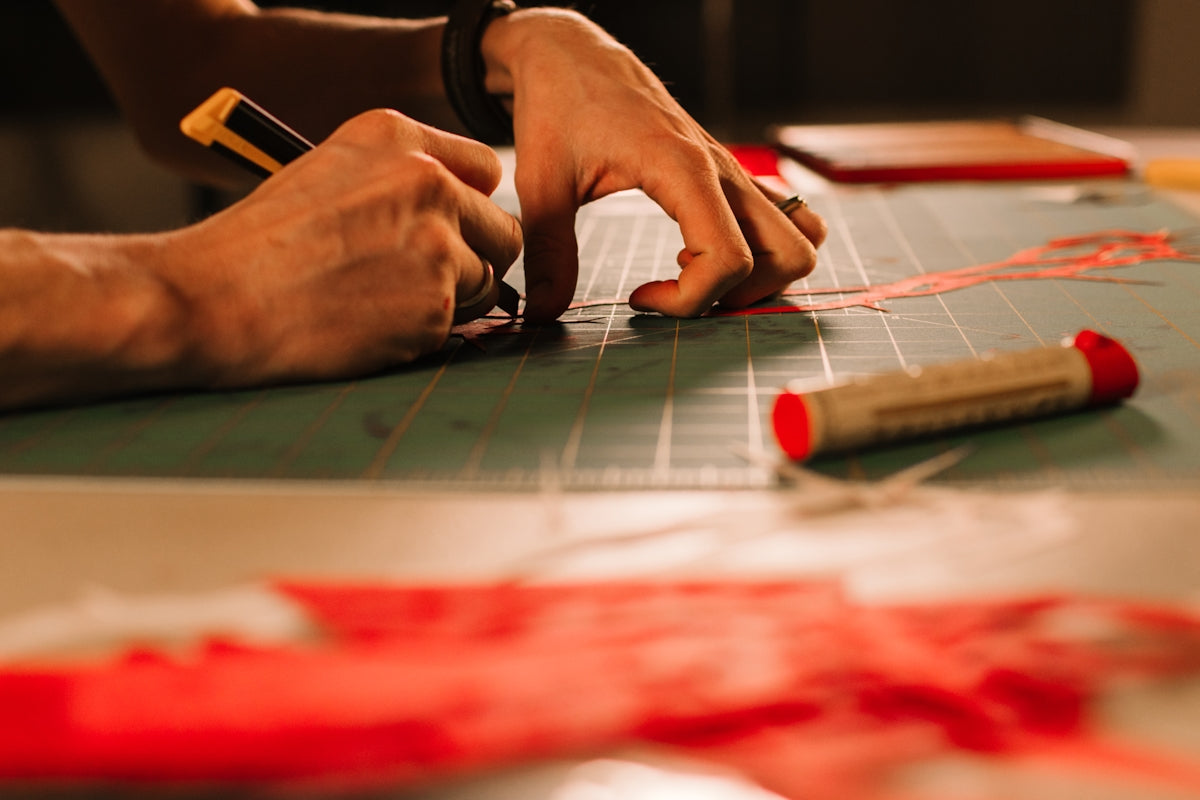 Hands using a craft knife to cut red material.